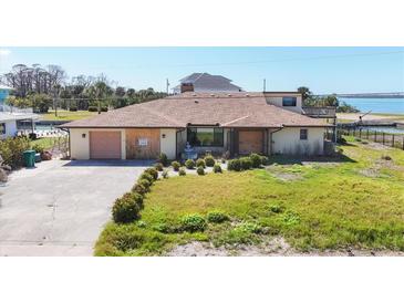 Exterior elevation of canal front home with 2-car garage and overgrown landscaping on a sunny day at 1905 Pennsylvania Ave, Englewood, FL 34224