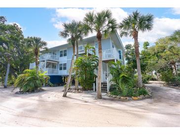 Charming three-story beach house with a light blue exterior, palm trees, and white railings at 7536 Palm Island S Dr # 1522, Placida, FL 33946