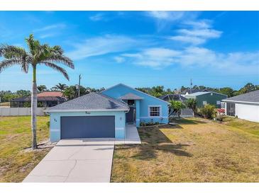 Exterior elevation of a one-story light blue home featuring a two-car garage, palm tree, and a well-manicured lawn at 12359 Deepwoods Ave, Port Charlotte, FL 33981