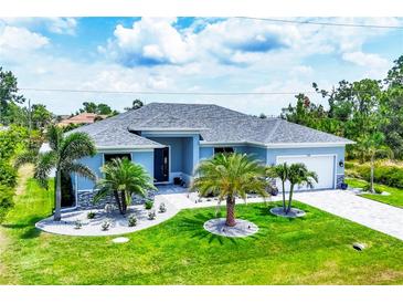Charming light blue home featuring a gray roof and manicured lawn with decorative palm trees at 13348 Boabadilla Ln, Port Charlotte, FL 33981