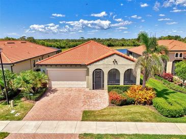 Charming single-story home featuring a red tile roof, arched entryway, lush landscaping, and a brick-paved driveway at 23590 Copperleaf Dr, Venice, FL 34293