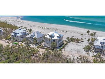 Aerial view of elegant beachfront homes with white metal roofs and manicured landscaping against a backdrop of turquoise ocean waters at 6890 Palm Island Dr, Placida, FL 33946