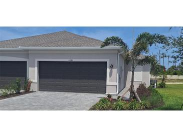 Exterior view of home featuring a gray two car garage, manicured landscaping, and a charming palm tree at 8661 Seasalt Loop, Englewood, FL 34224