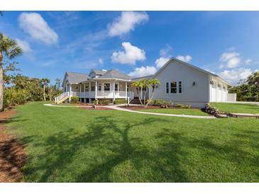 Beautiful white two-story home with a well-manicured lawn and a charming wraparound porch at 9144 Spring Valley Rd, Englewood, FL 34224