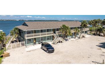 Two-story building featuring multiple units, surrounded by palm trees, water views and a car parked in the expansive parking area at 5041 N Beach Rd # 2A And 2B, Englewood, FL 34223