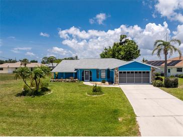Charming blue home featuring a lush lawn, gray roof, stone accents, and well-maintained landscaping at 23 Bunker Cir, Rotonda West, FL 33947