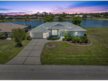 Scenic view of a home on the water at sunset, with a lush lawn and a driveway leading to an attached garage at 9064 Bantry Bay Blvd, Englewood, FL 34224