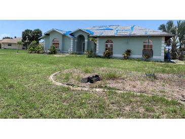 Exterior view of a single-story home needing repairs, with a neglected lawn and blue tarp on the roof at 1 Clubhouse Rd, Rotonda West, FL 33947