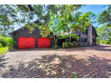 Inviting home with a brick driveway, red garage doors, and a striking stone chimney at 1550 Bayshore Dr, Englewood, FL 34223