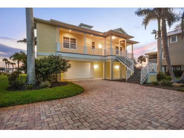 Charming two-story yellow home features a brick driveway, covered porch, and attached garage at 1784 Bayshore Dr, Englewood, FL 34223