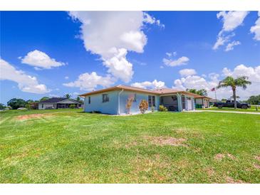 Well-maintained single-story home with a large, green lawn and light blue exterior under a clear blue sky at 7437 Bass St, Englewood, FL 34224
