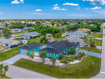 Aerial view of a vibrant turquoise home featuring a well-maintained lawn and lush landscaping at 9457 Heartwellville Ave, Englewood, FL 34224