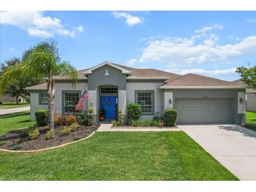 Charming single-story home with a manicured lawn, lush landscaping, and a vibrant blue front door at 13365 Chesapeake Pl, Spring Hill, FL 34609