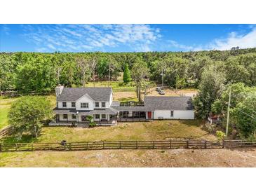 Sprawling two-story white farmhouse with a stone chimney, front porch and expansive grounds at 8922 Pritcher Rd, Lithia, FL 33547