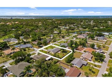 An aerial view of a quaint home with a large yard surrounded by lush greenery and other homes in a tranquil neighborhood at 566 Viridian St, Englewood, FL 34223