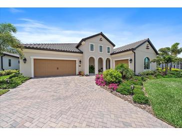 Elegant stucco home featuring a paver driveway, tile roof, lush landscaping and a three-car garage at 284 Bocelli Dr., Nokomis, FL 34275