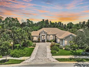 Stunning single-story home with lush landscaping, a brick driveway, and a tile roof under a captivating sunset sky at 4376 Corso Venetia Blvd, Venice, FL 34293