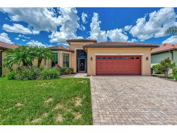 Tan house with red garage door, lush landscaping, and paved driveway at 20193 Pezzana Dr, Venice, FL 34292