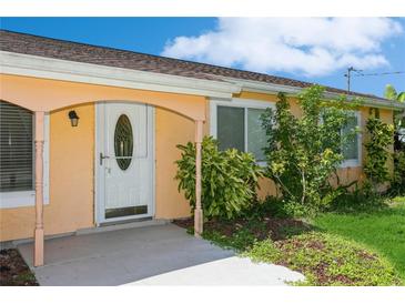 Quaint light orange home with white door and lush landscaping at 18069 Ohara Dr, Port Charlotte, FL 33948
