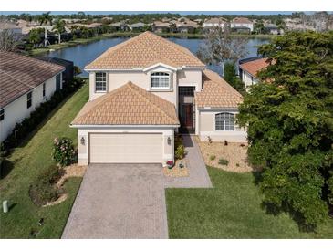 Two-story house with tile roof, two-car garage, and a landscaped yard near a lake at 11614 Dancing River Dr, Venice, FL 34292