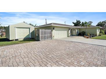 Light green house with a brick driveway, two-car garage and storage shed at 1072 Venetian Pkwy, Venice, FL 34285