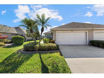 Exterior view of a light beige villa with a two-car garage, lush landscaping, and palm trees at 3897 Fairway Dr, North Port, FL 34287