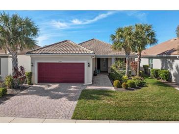 Single-story home with red garage door, landscaped yard, and paver driveway at 19397 Rizzuto St, Venice, FL 34293