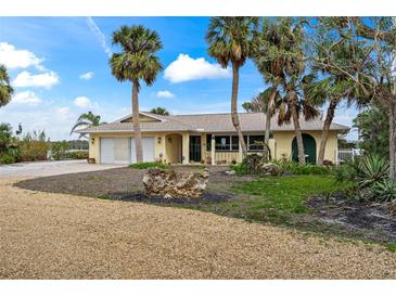 Charming single-story home features a two-car garage, lush landscaping with palm trees, and a sunny gravel driveway at 7825 Manasota Key Rd, Englewood, FL 34223