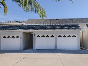 A row of garages with white doors and a grey tiled roof, under a sunny, blue sky at 936 Capri Isles Blvd # 102, Venice, FL 34292