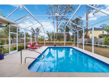 Beautiful screened-in pool area with two red lounge chairs, clear blue water, and stainless steel handrail at 1684 Ruiz St, North Port, FL 34286