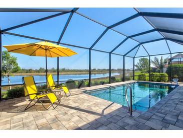 Screened pool with waterfront view, lounge chairs and sun umbrella on brick paver patio at 10466 Medjool Dr, Venice, FL 34293