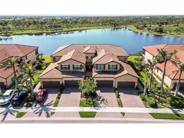 Stunning aerial view of a residential building with a tile roof situated near a serene lake and lush greenery at 10797 Tarflower Dr # 202, Venice, FL 34293