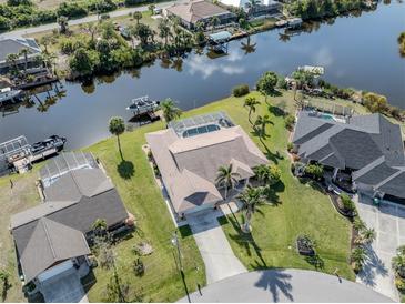 Waterfront home featuring a screened-in pool, boat dock, and lush landscaping on a sunny day at 9542 Spring Cir, Port Charlotte, FL 33981