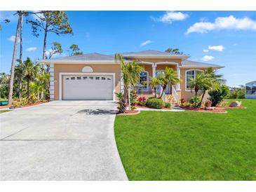 Charming tan home featuring a spacious two-car garage, manicured lawn, and beautifully landscaped front yard at 951 Sea Fox Rd, Venice, FL 34293