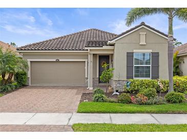 Charming home featuring a tile roof, brick driveway, manicured landscaping, and a two-car garage at 11655 Renaissance Blvd, Venice, FL 34293