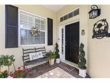 Inviting front porch with a black front door, Welcome mat, and decorative plants and bench at 1627 Lancashire Dr, Venice, FL 34293