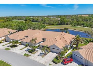 Stunning aerial view of attached villa homes with tile roofs, lush landscaping, a pond, and a golf course nearby at 1853 San Silvestro Dr, Venice, FL 34285