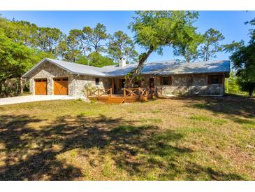 Charming stone house featuring a metal roof, wood-accented garage doors, and a cozy wooden porch at 8902 Tropicaire Blvd, North Port, FL 34291