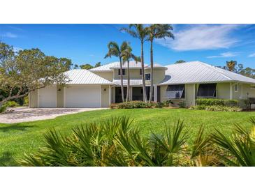 Stunning home features a metal roof, three-car garage, and lush landscaping with palm trees against a clear blue sky at 1657 Bayshore Dr, Englewood, FL 34223