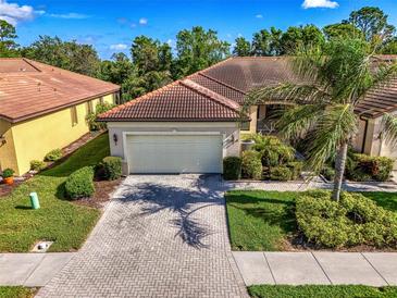 Beautiful villa with a paver driveway, tile roof, well-manicured lawn, and lush landscaping at 11096 Campazzo Dr, Venice, FL 34292