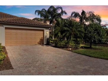 Beautiful exterior view with a two-car garage, tile roof, brick drive, and palm trees against a colorful sunset at 115 Babbling Brook Run, Bradenton, FL 34212