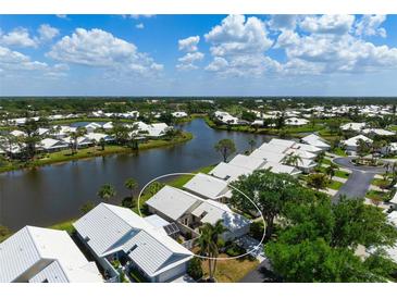 An aerial view of a lakeside home with white roof, lush landscaping, and serene water views at 799 Harrington Lake N Dr # 73, Venice, FL 34293