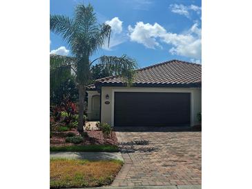 Charming home featuring a clay tile roof, brick driveway and tropical landscaping with a palm tree in front at 20188 Tesoro Dr, Venice, FL 34293