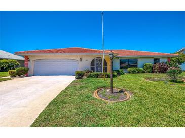 Charming single-story home with a well-manicured lawn, an attached garage, and a vibrant red tile roof at 322 Oakwood Cir, Englewood, FL 34223