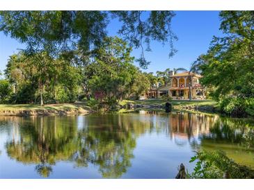 Stunning view of estate home overlooking a serene pond surrounded by mature trees on a sunny day at 2750 Gocio Road Ext, Sarasota, FL 34235