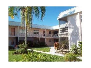 Two-story condo building featuring white exterior, balconies, green lawn, and mature trees, offering a serene living environment at 400 Base # 225, Venice, FL 34293