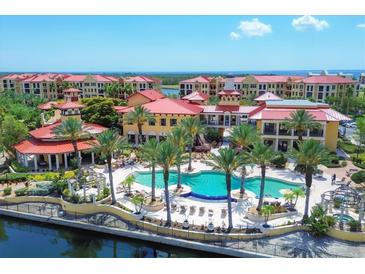 Stunning aerial view of the community pool and clubhouse with palm trees and ocean views beyond the red tile roofs at 97 Vivante Blvd # 306, Punta Gorda, FL 33950