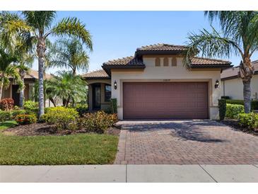 Charming home features a two-car garage, tile roof, lush landscaping, and a brick paver driveway at 13829 Alafaya St, Venice, FL 34293