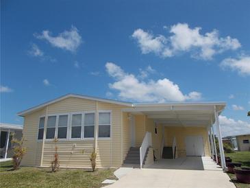 Charming, light yellow single-Gathering home with attached carport, lush green grass, and bright blue sky at 554 Aspen Ave, Venice, FL 34285
