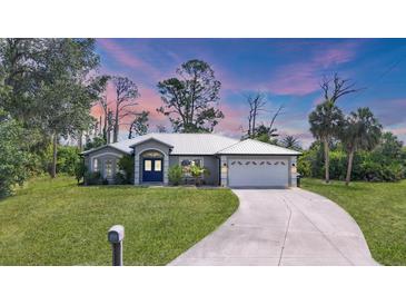 Beautiful home with a metal roof, manicured lawn, and a long driveway leading to a two-car garage at 1214 Rumson Ct, North Port, FL 34288